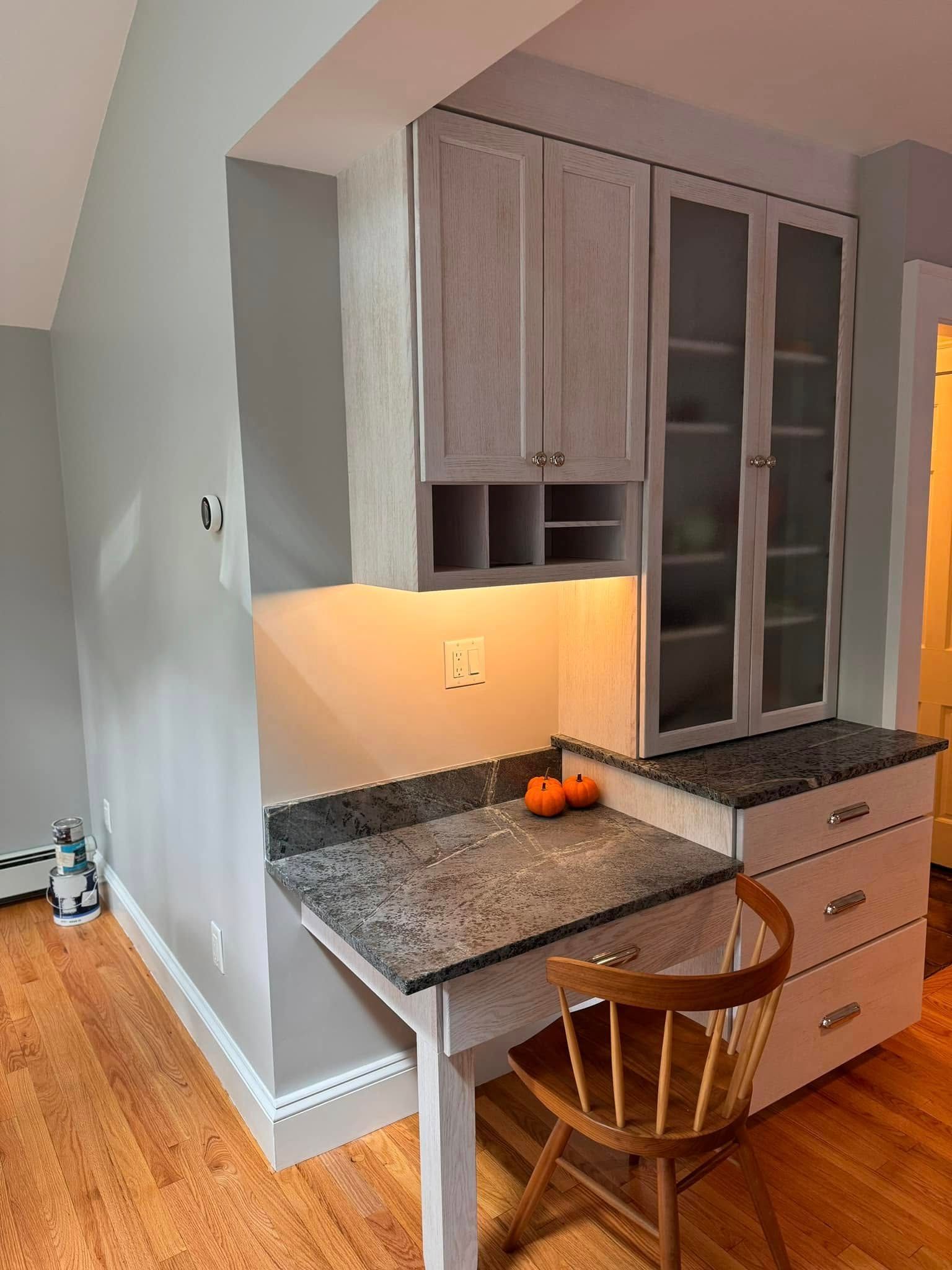 A kitchen with a desk, chair, and cabinets.