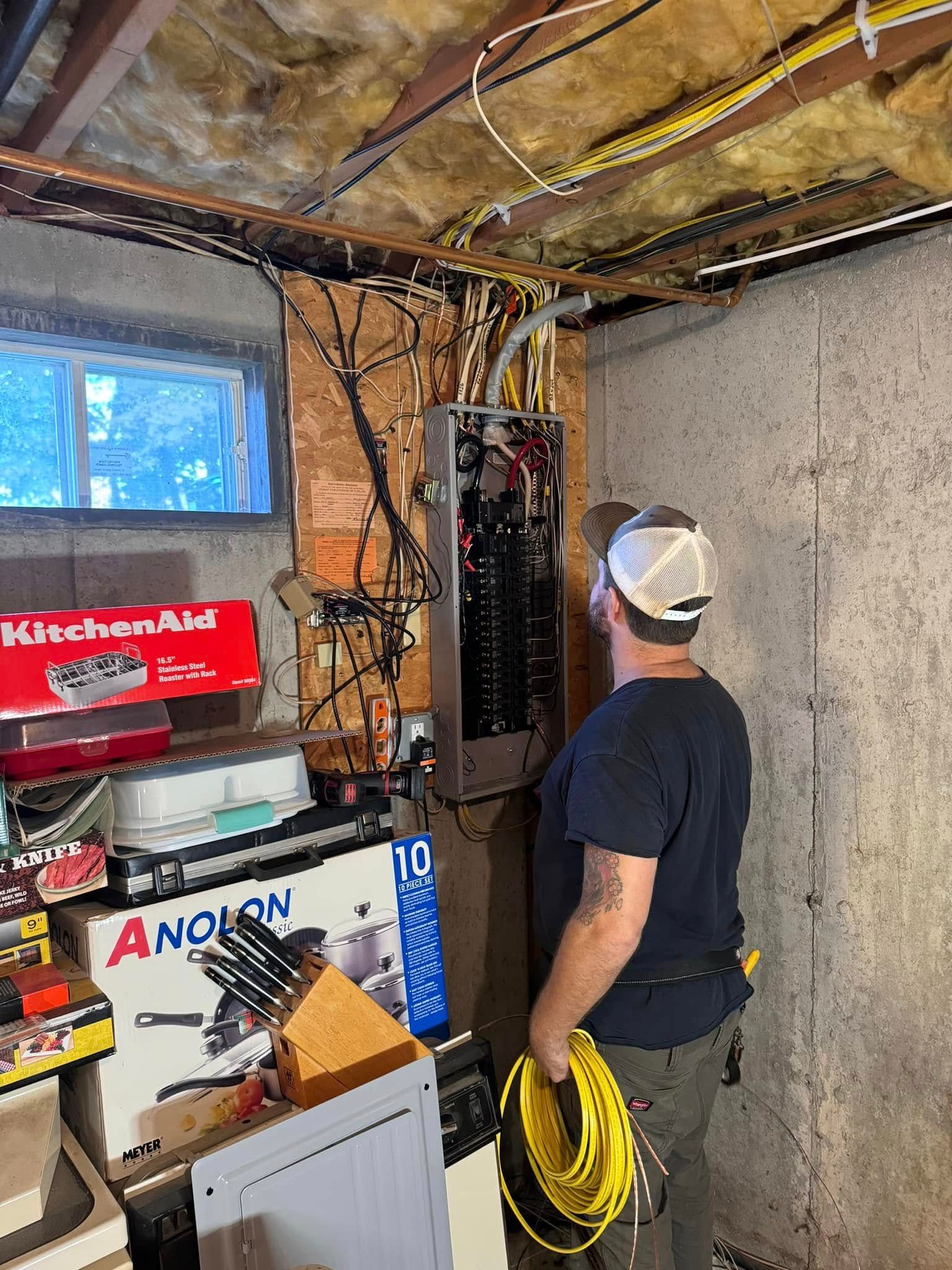 A man is standing in a basement looking at a electrical box.
