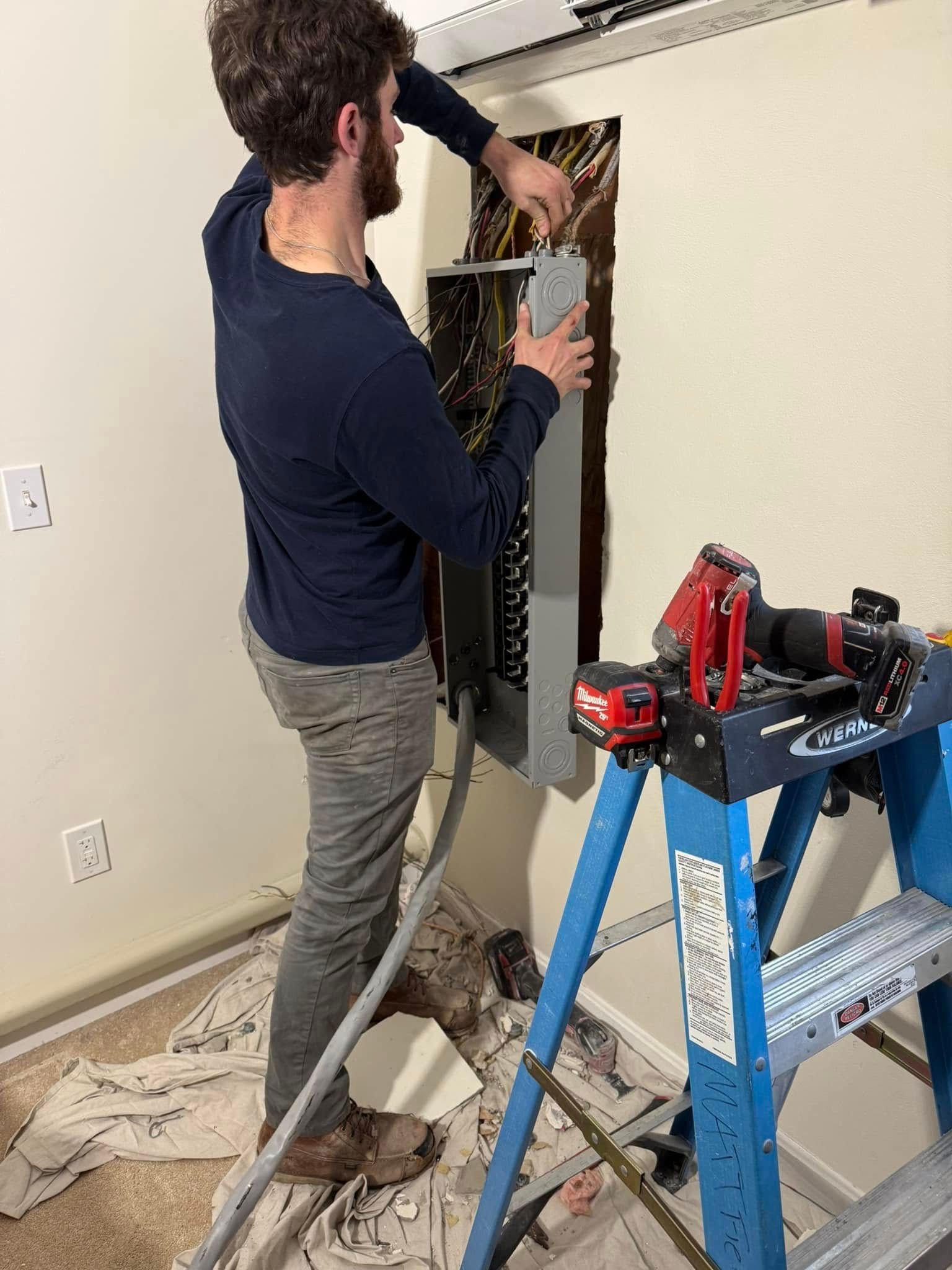 A man is standing next to a blue ladder working on a wall.