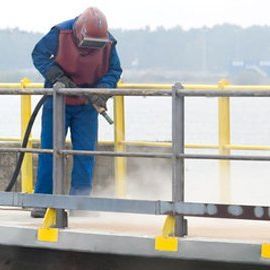 A man wearing a helmet is sandblasting a fence.