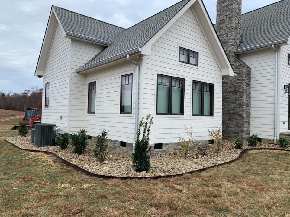 A white house with a gray roof and black windows is sitting on top of a lush green field.