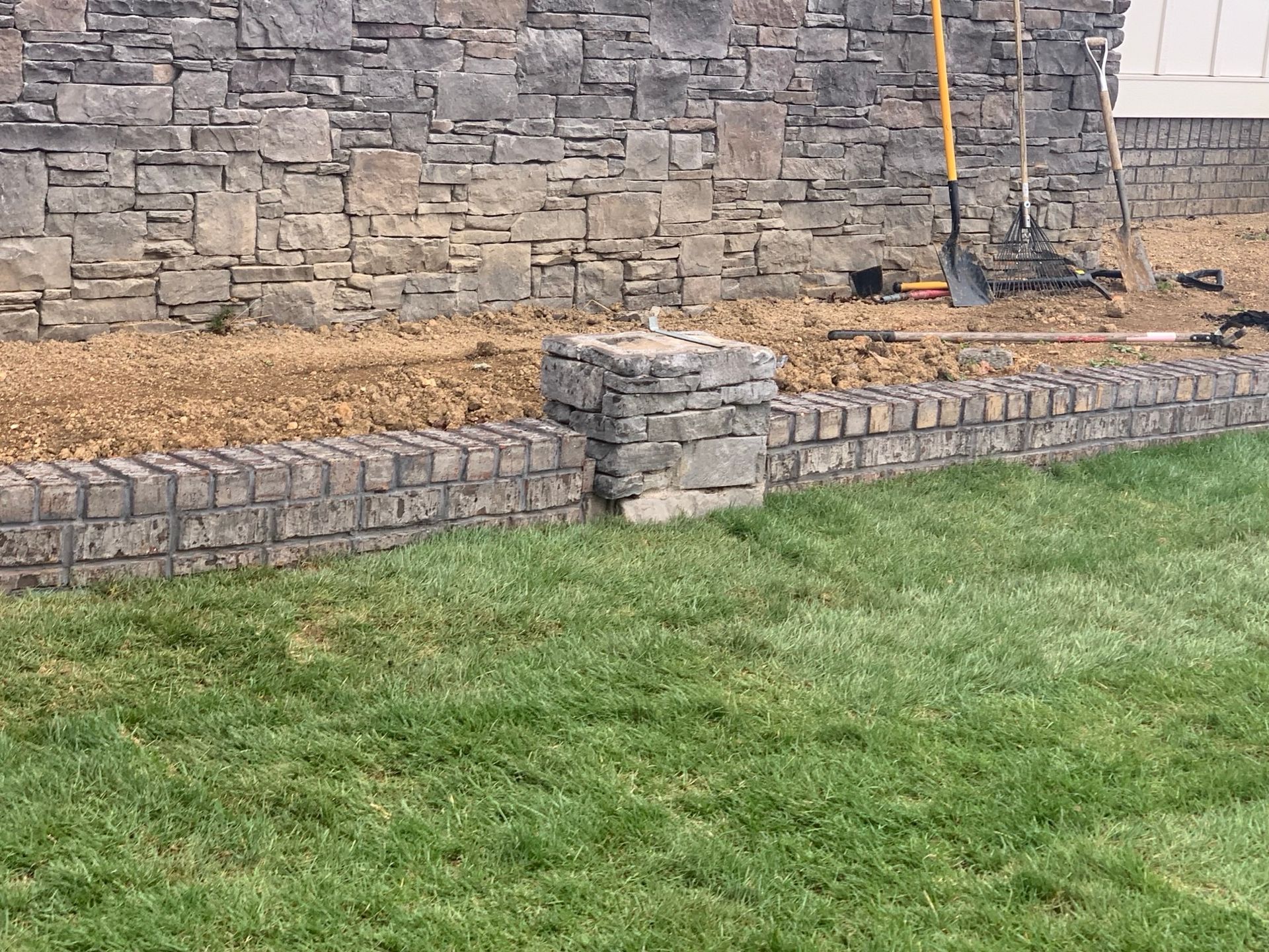 A stone wall surrounds a lush green lawn in front of a house.