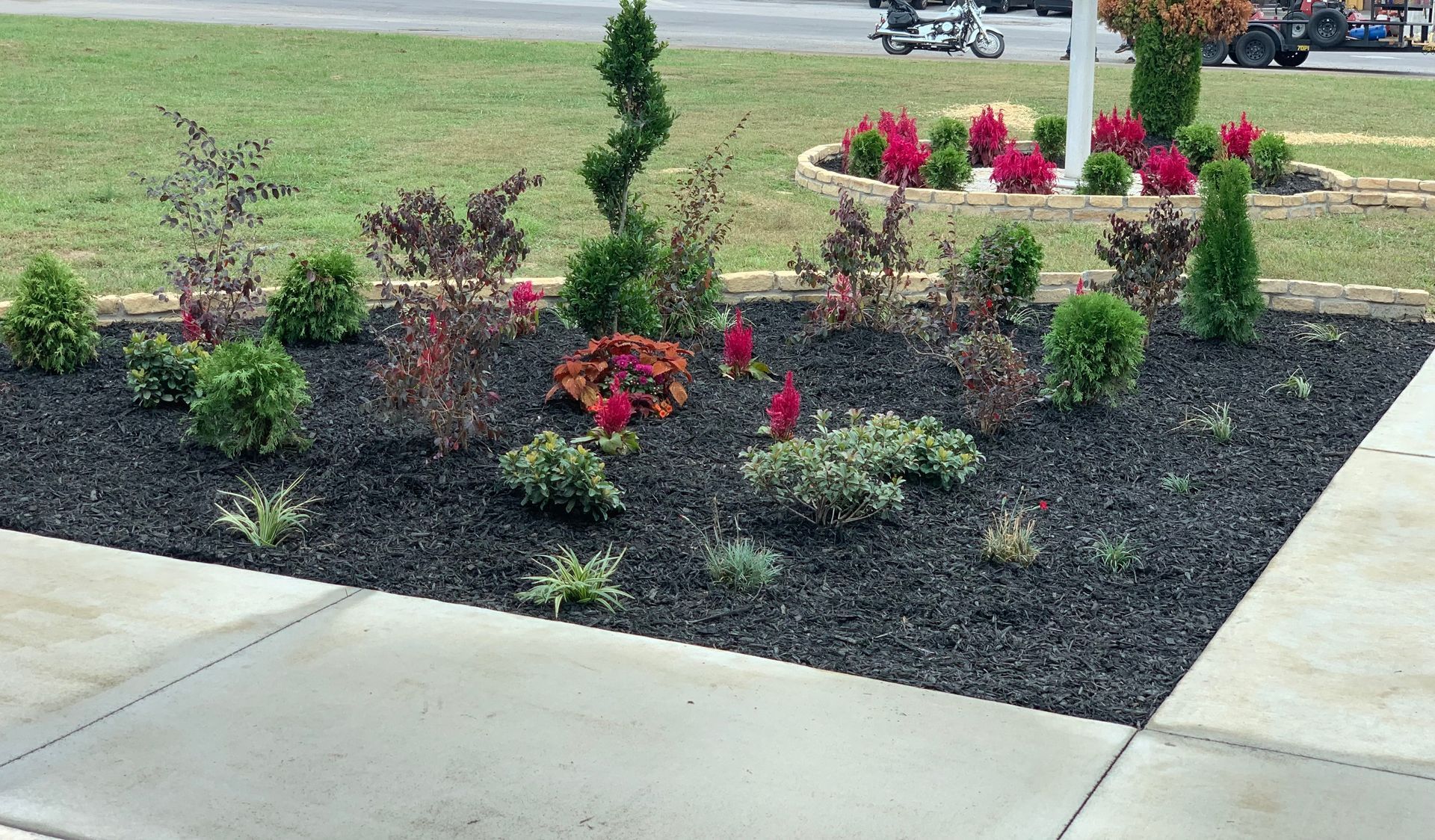 A garden with flowers and shrubs on a sidewalk next to a sidewalk.