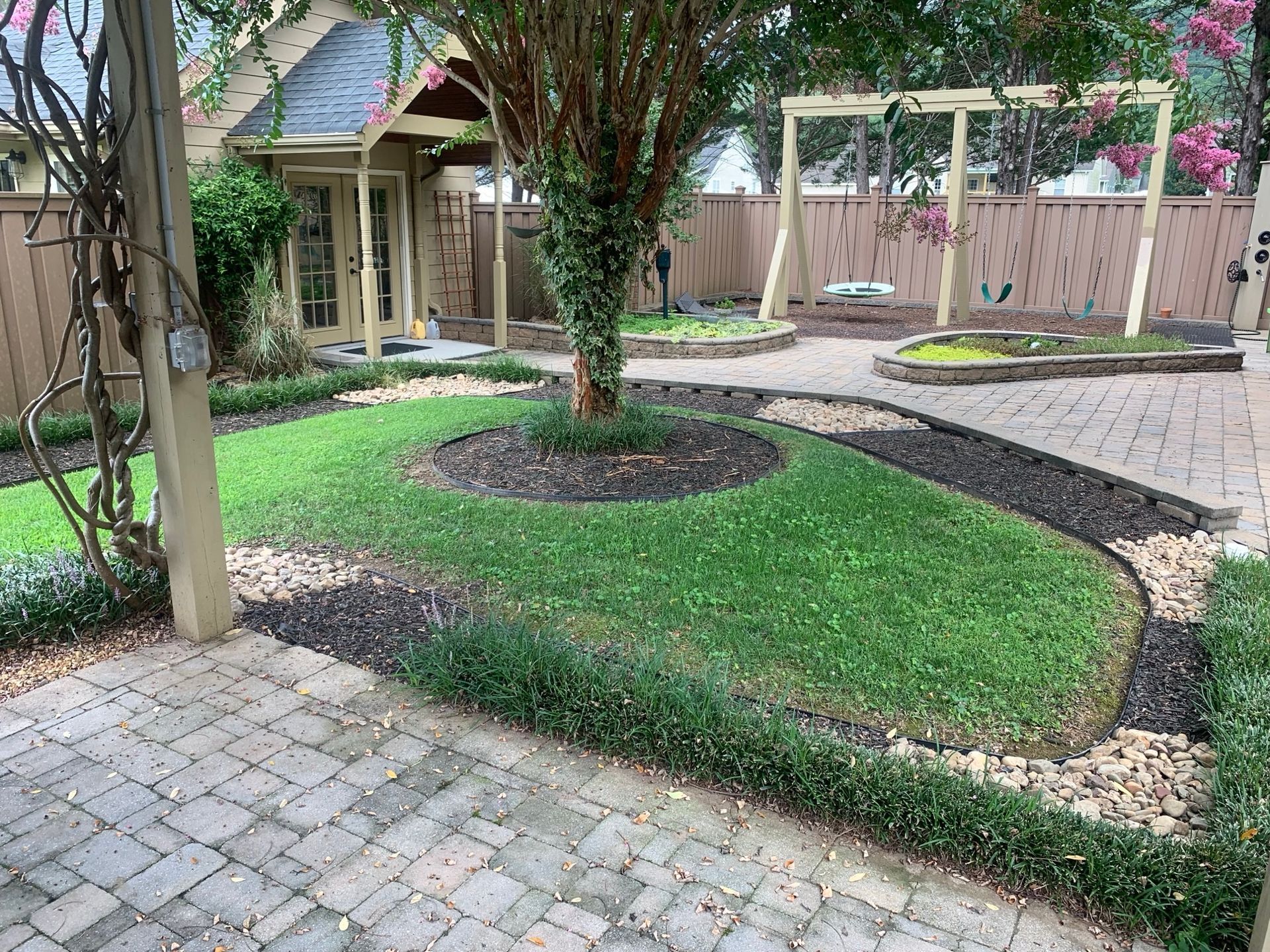 A brick walkway leading to a house with a tree in the middle of the yard.