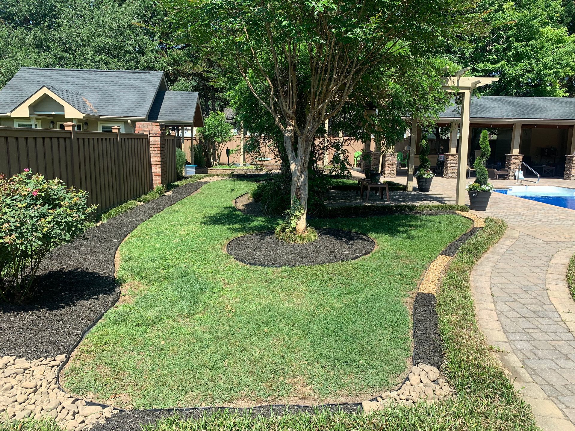 A lush green lawn in front of a house with a pool.