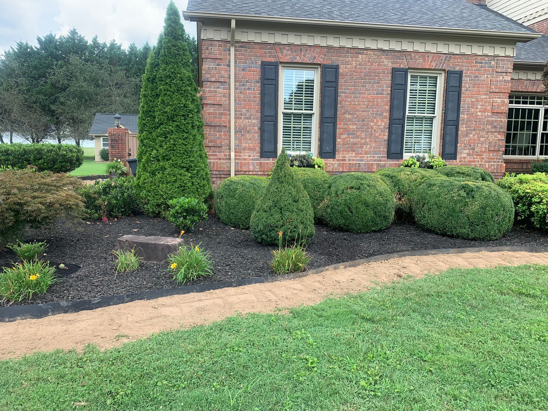 A brick house with black shutters and bushes in front of it.