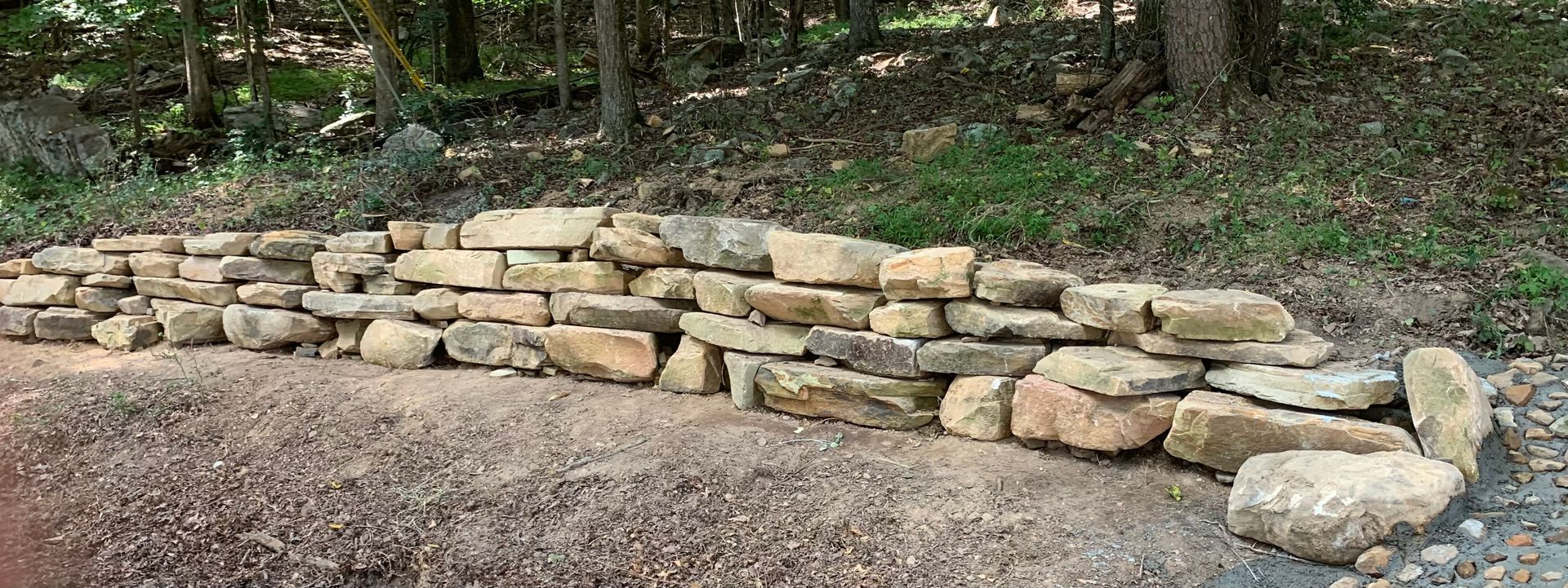 A stone wall is sitting on the side of a dirt road in the woods.