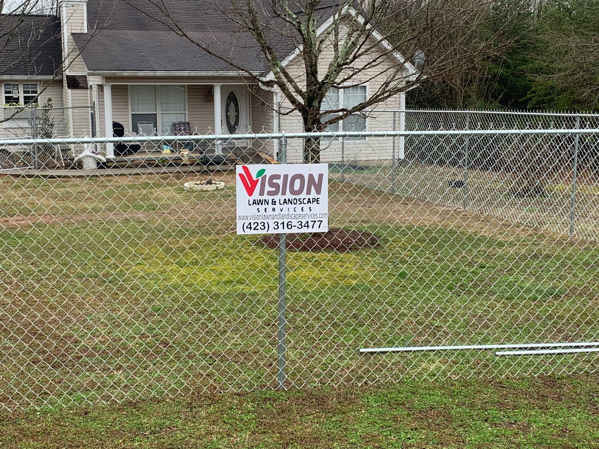 A chain link fence with a vision sign in front of a house.