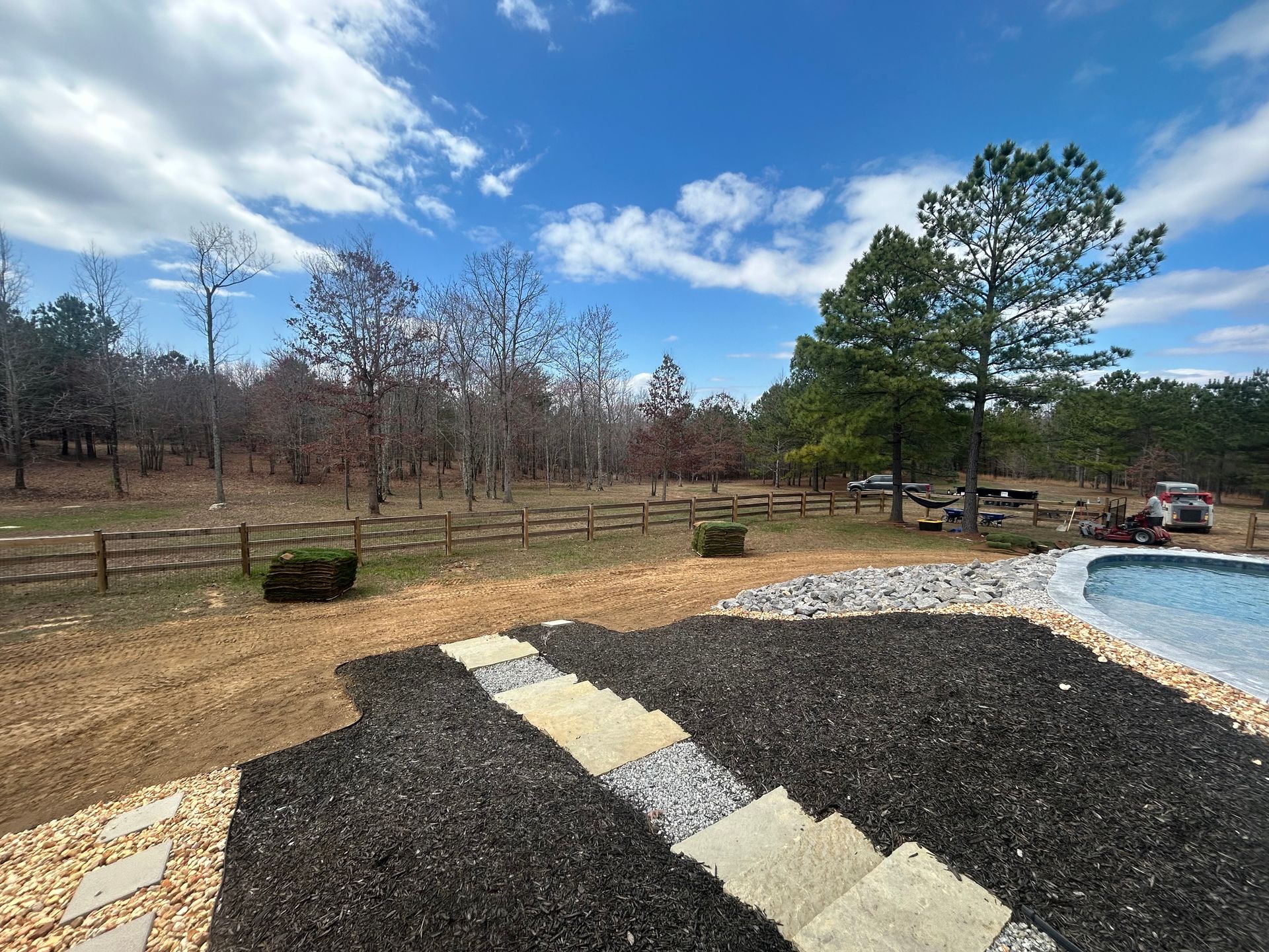 A fenced in yard with a pool and trees in the background.