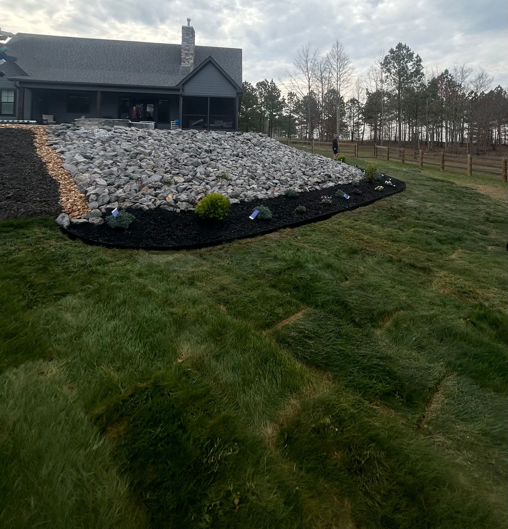 A large lawn with a house in the background and a large pile of rocks in the foreground.