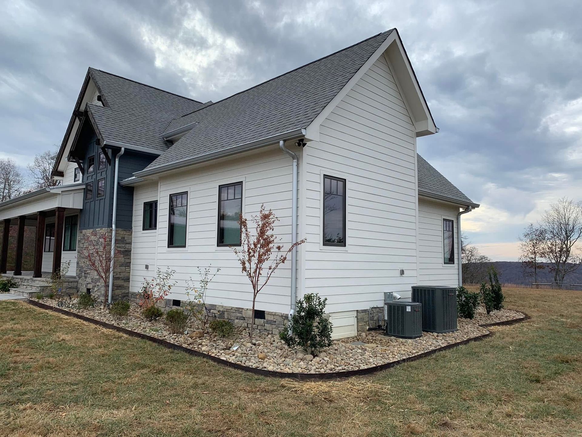 A white house with a gray roof is sitting on top of a lush green field.