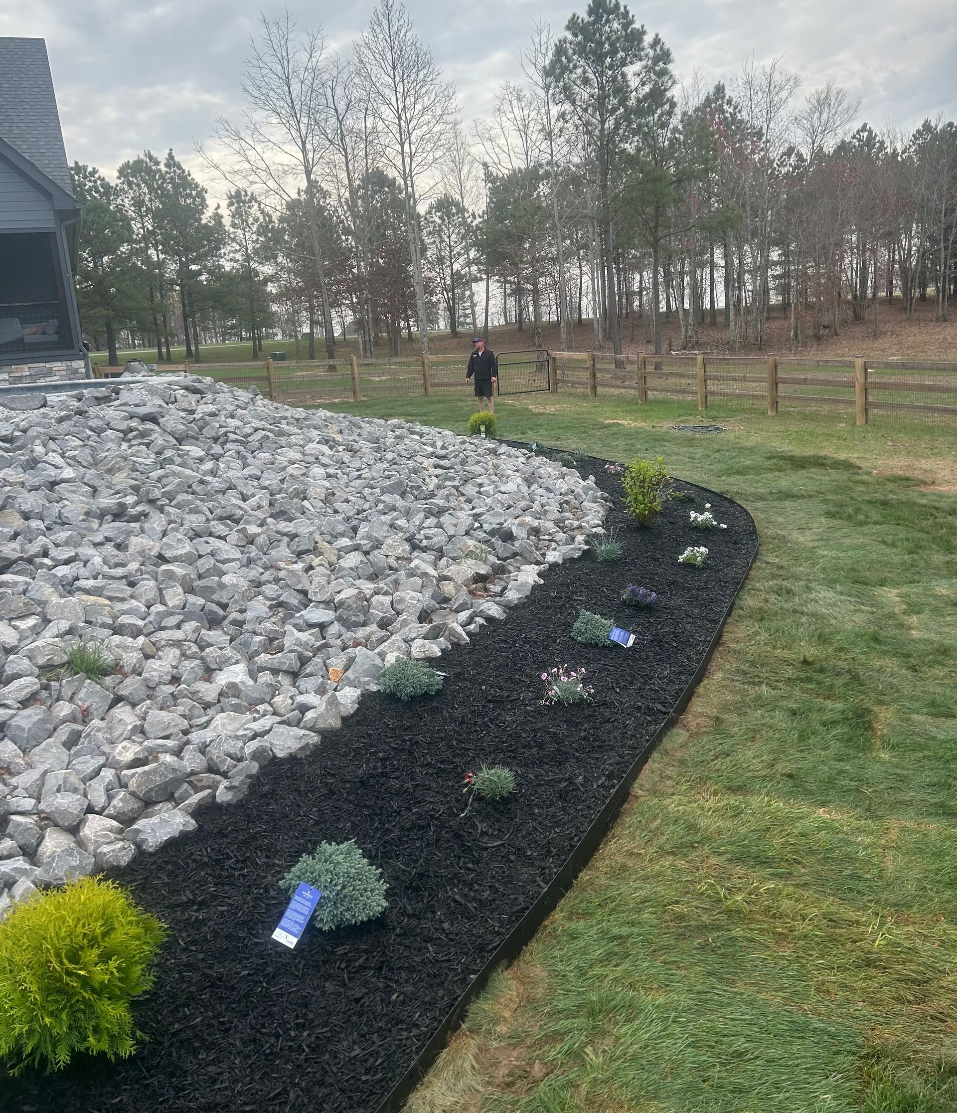 A man is standing in a yard next to a pile of rocks.