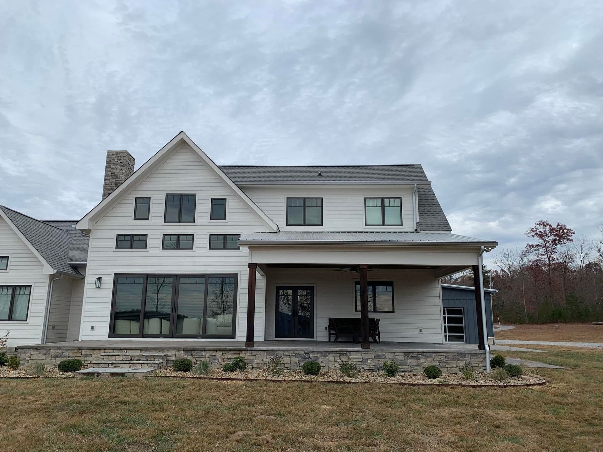 A large white house with a gray roof is sitting on top of a lush green field.