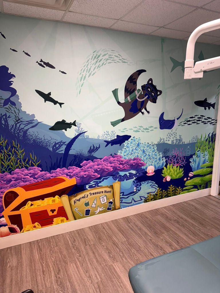 Underwater vinyl wall wrap with a raccoon diver, treasure chest, and fish, in a dental office.