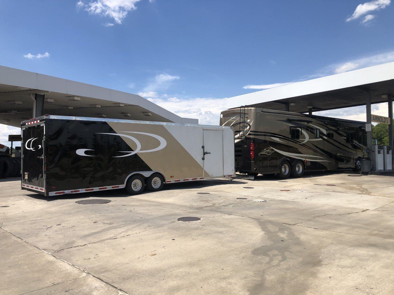 A trailer is being towed by a rv at a gas station.