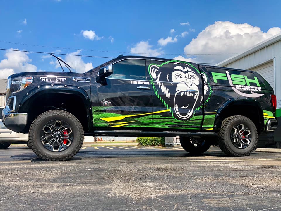 A black truck with a green monkey on the side is parked in a parking lot.