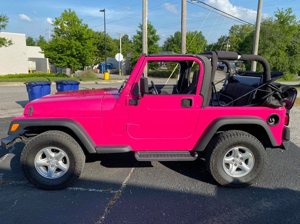 A pink jeep is parked in a parking lot.
