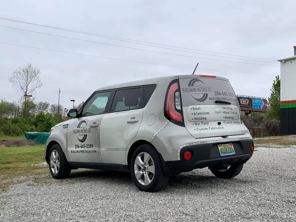 A white car is parked in a gravel lot in front of a building.