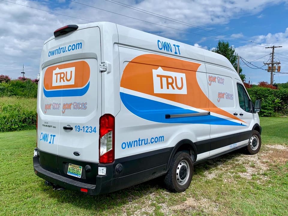 A white and orange van is parked in a grassy field.