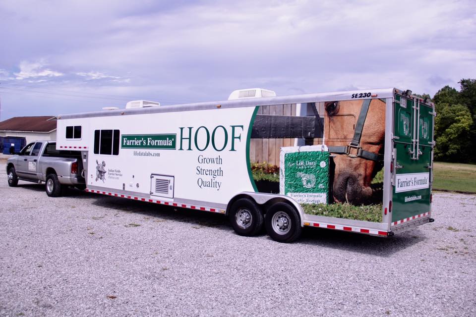A trailer with a picture of a horse on it is parked next to a truck.