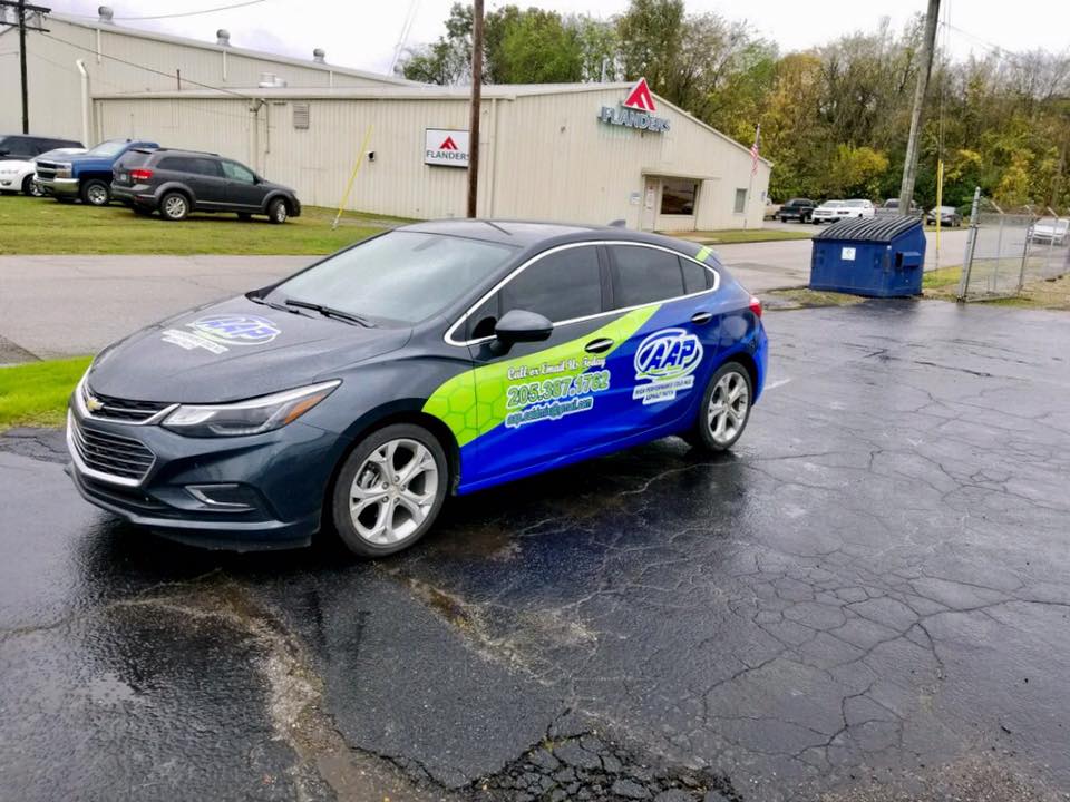 A blue and yellow car is parked in a parking lot in front of a building.