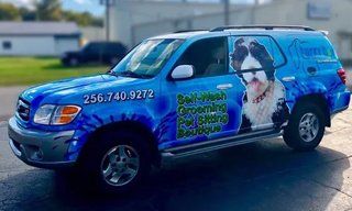 A blue suv with a dog on the side is parked on the side of the road.