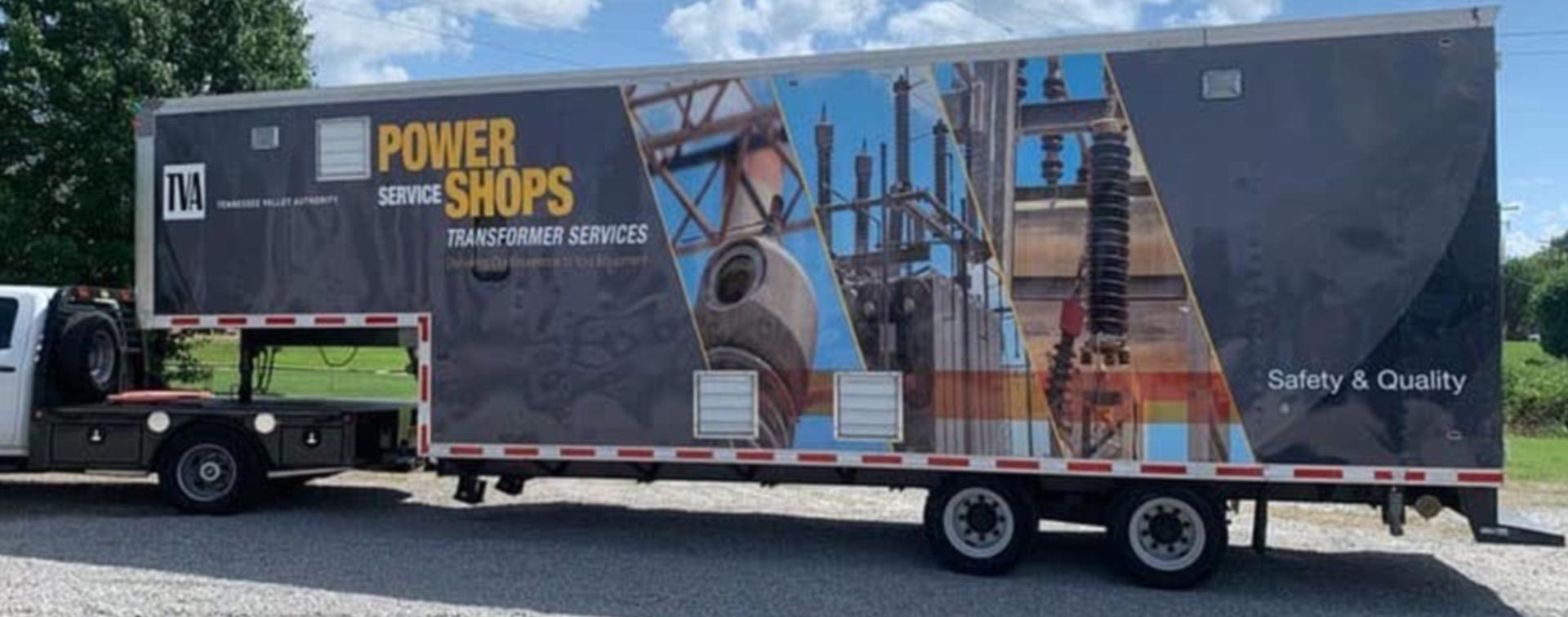 A large truck with a trailer attached to it is parked in a gravel lot.