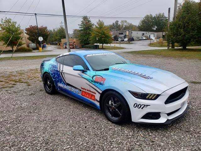 A blue and white mustang is parked in a gravel lot.