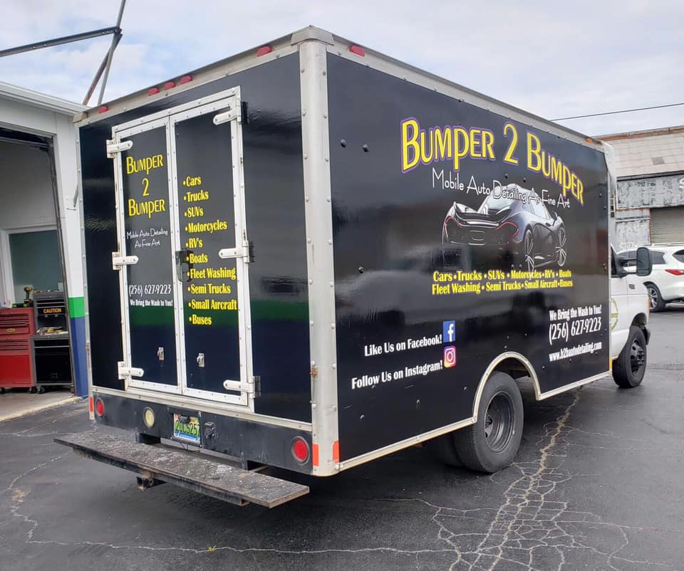 A bumper 2 bumper truck is parked in front of a garage.