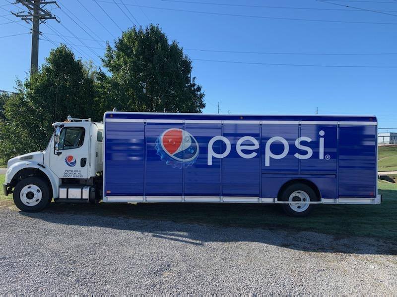 A blue and white pepsi truck is parked in a gravel lot.