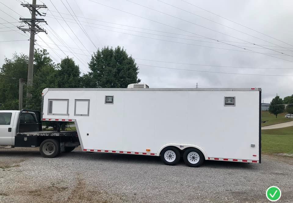 A white trailer is being towed by a black truck.