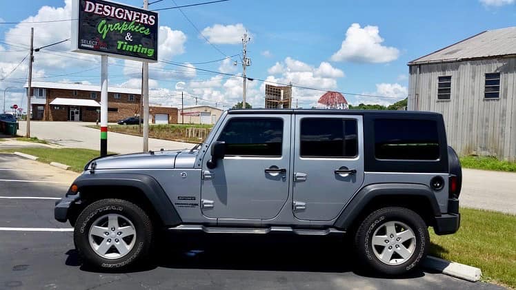A silver jeep is parked on the side of the road in front of a sign.