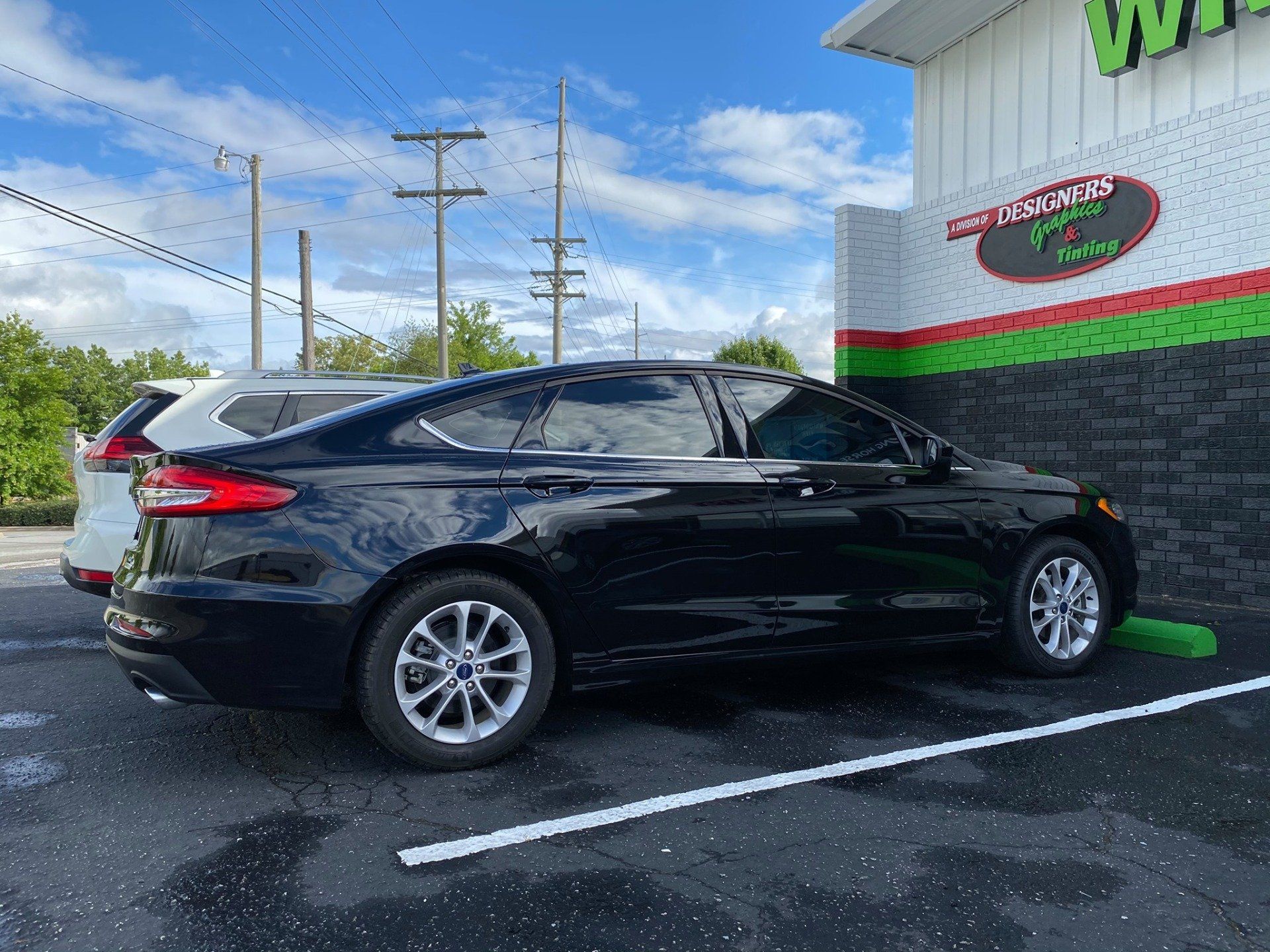 A black car is parked in a parking lot in front of a building.