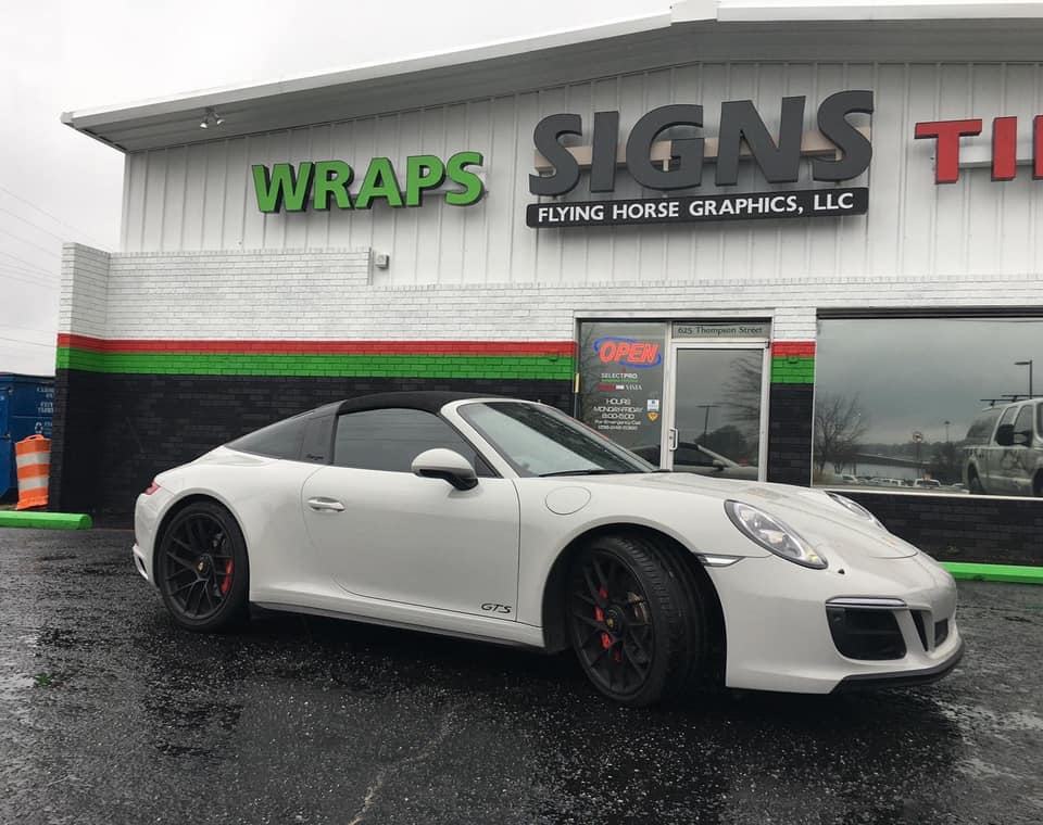 A white porsche targa is parked in front of a signs store.