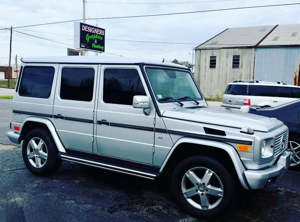 A silver suv is parked in front of a building with a sign that says designer graphics