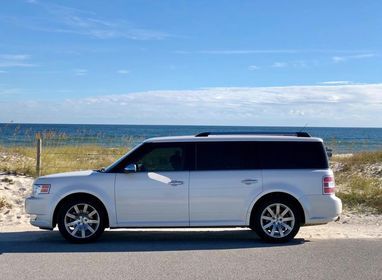 A white suv is parked on the side of the road near the ocean.