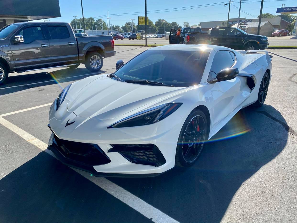 A white corvette is parked in a parking lot next to a truck.