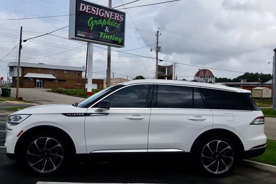 A white suv is parked in front of a sign for designers graphics and tinting.