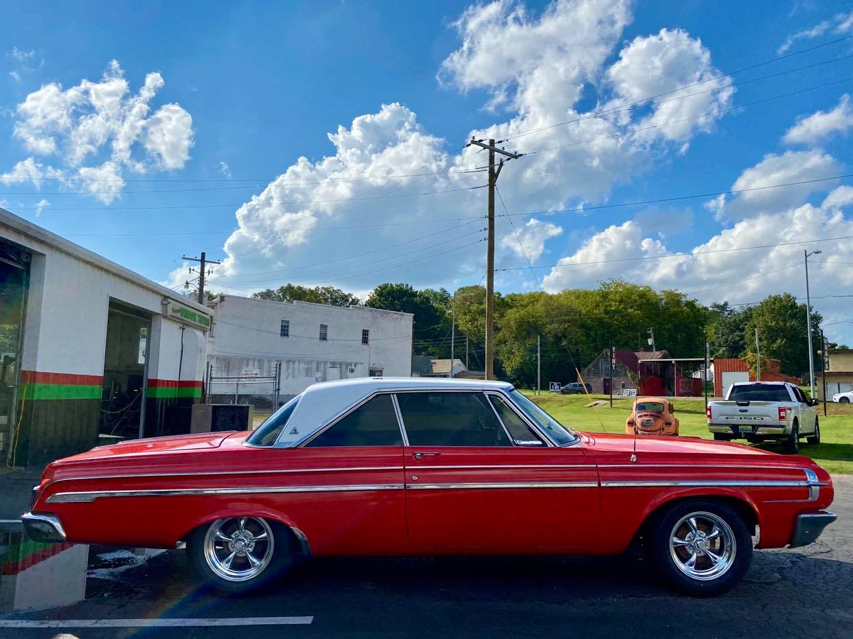 A red car is parked in a parking lot in front of a building.