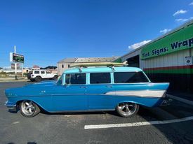 A blue car with a surfboard on top of it is parked in a parking lot.