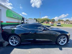 A black car is parked in front of a tire shop.