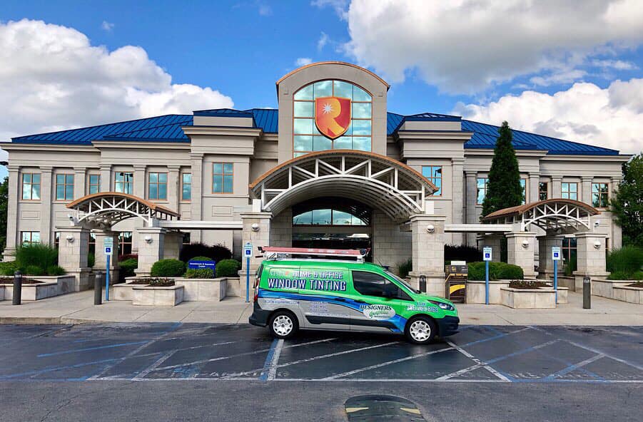 A green van is parked in front of a large building.
