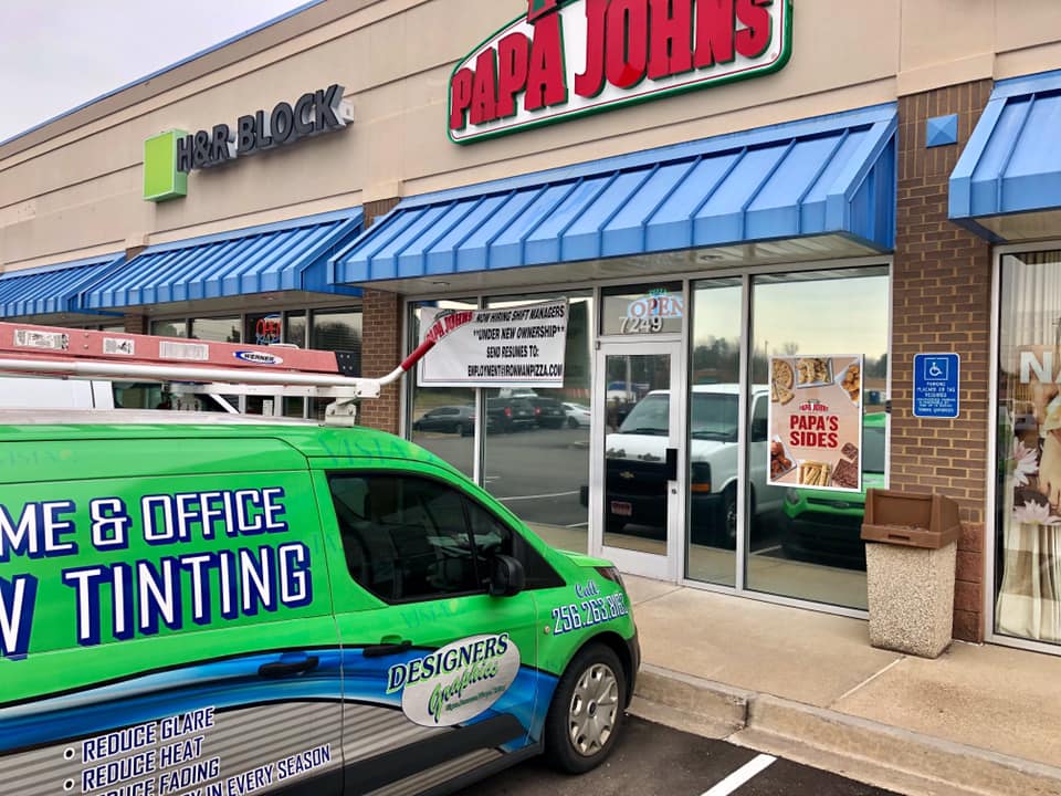A green van is parked in front of a papa john's restaurant.