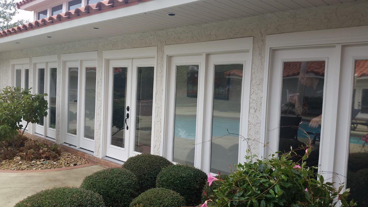 A white house with a lot of windows and shrubs in front of it.