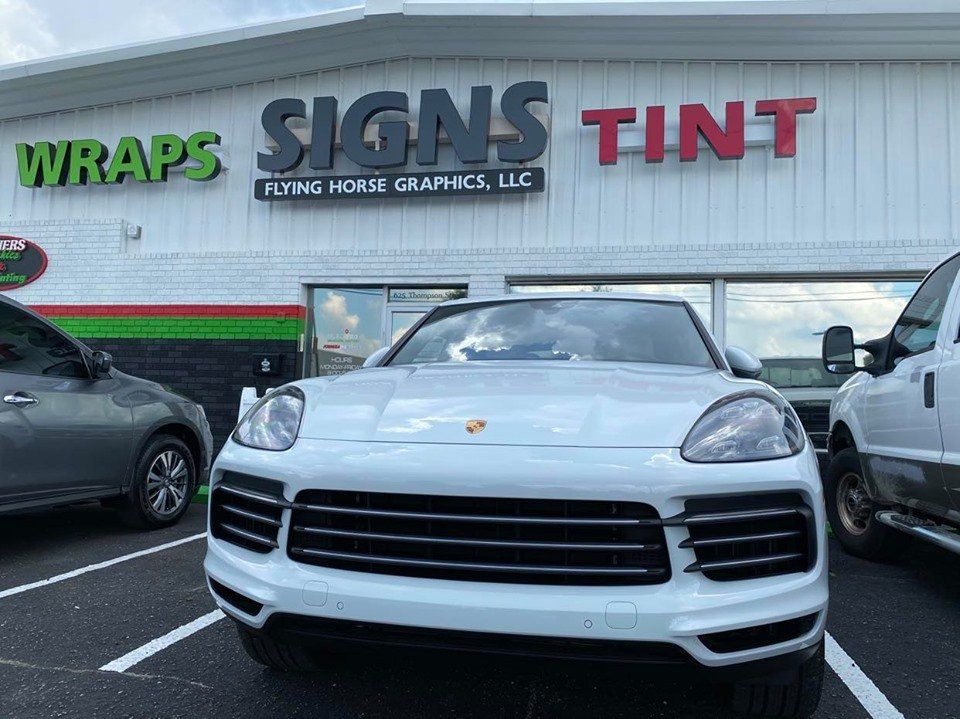 A white car is parked in front of a building that says signs tint.