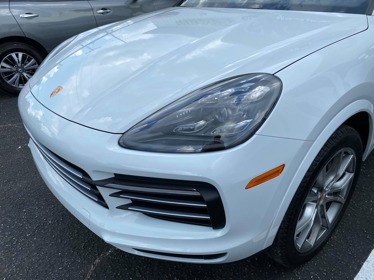 A white porsche cayenne is parked in a parking lot.