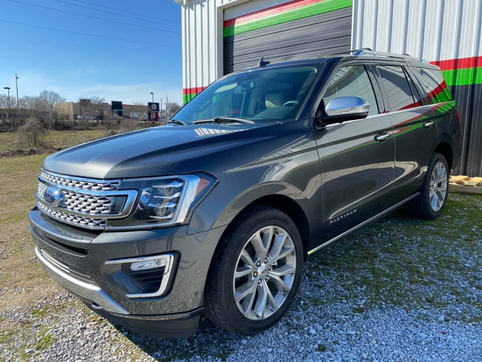 A gray ford expedition is parked in front of a building.