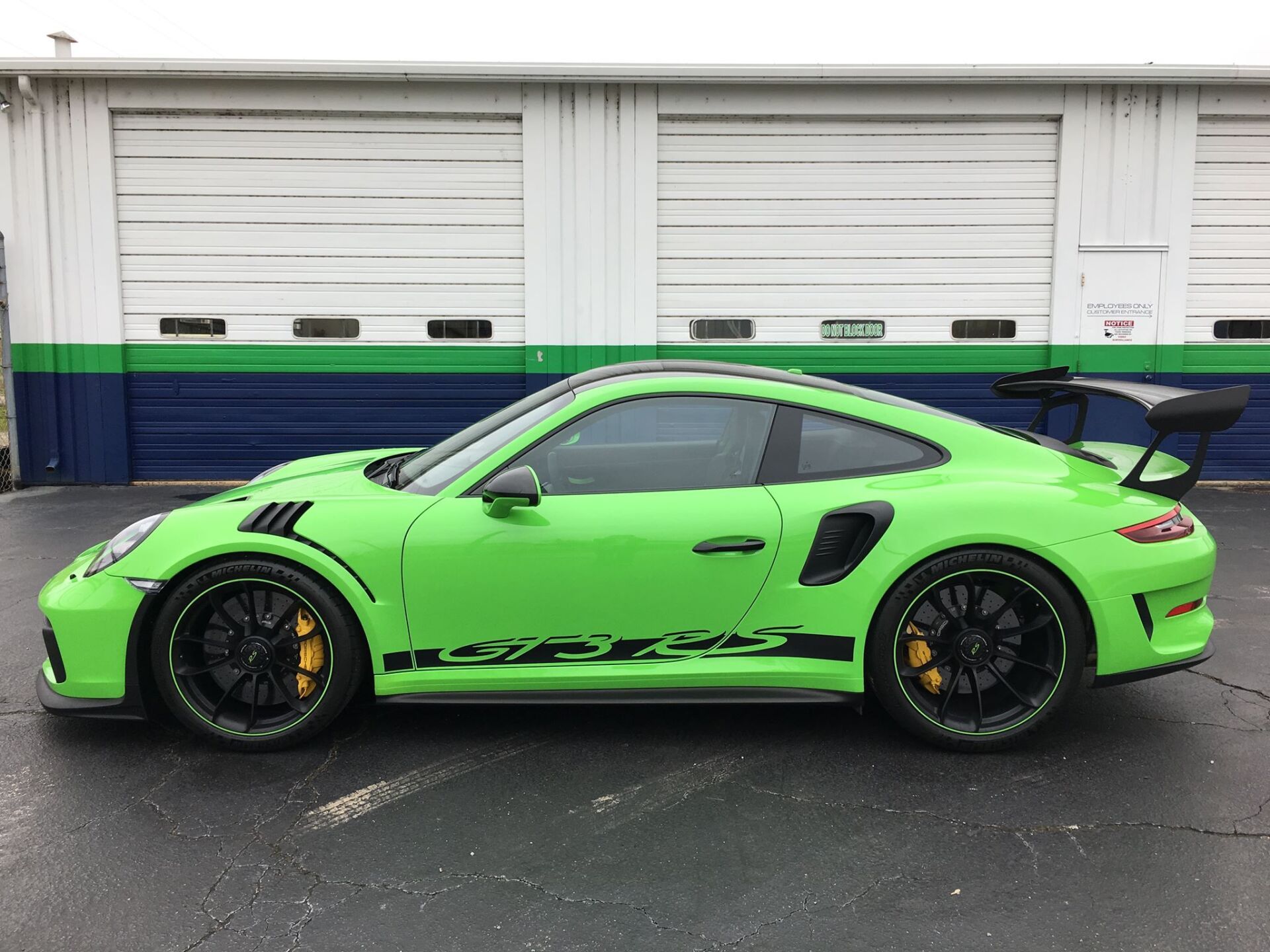 A green porsche 911 gt3 rs is parked in front of a garage.