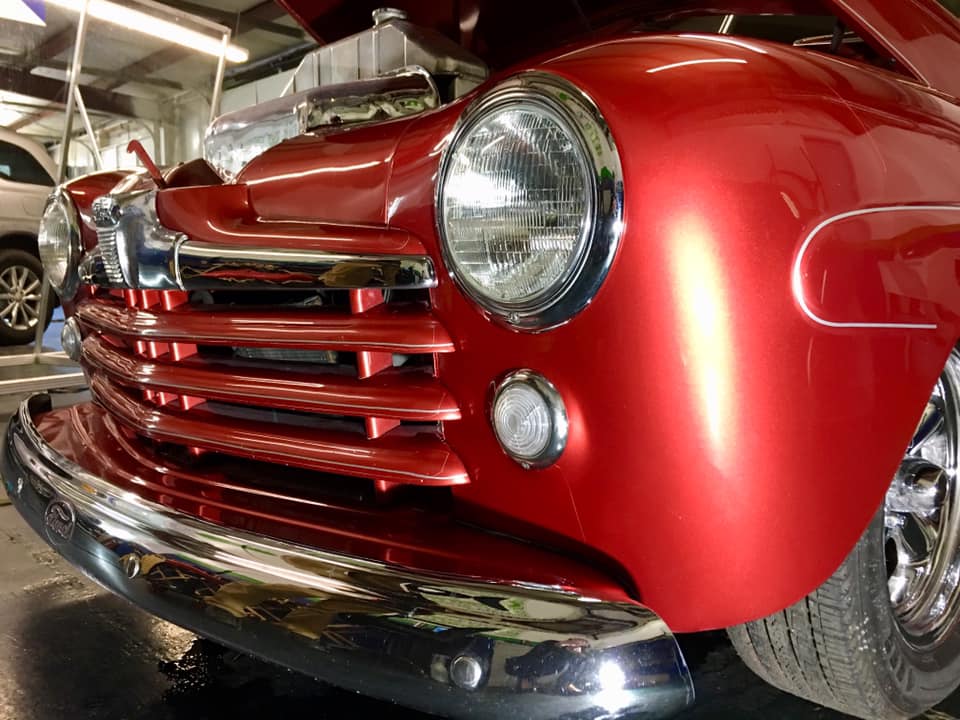 A red car with the hood up is parked in a garage.