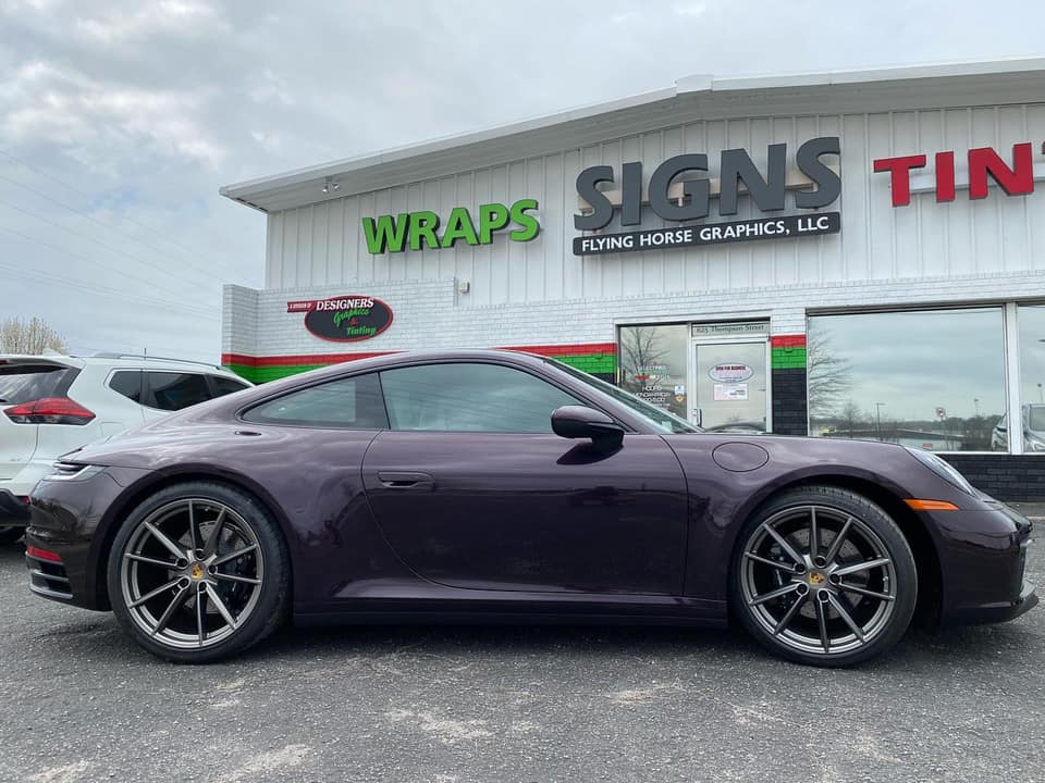 A purple porsche 911 is parked in front of a building.